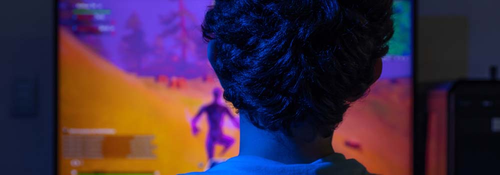 Osoba ogląda grę wideo na ekranie. Postać w grze biegnie po żółtym terenie z fioletowymi drzewami.