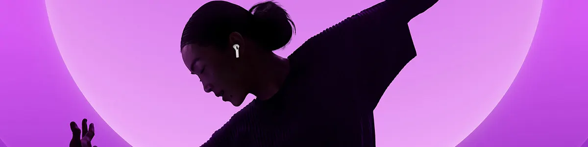 Kobieta z kokiem na głównym tle, w uszach na AirPodsy, a tło jest różowe