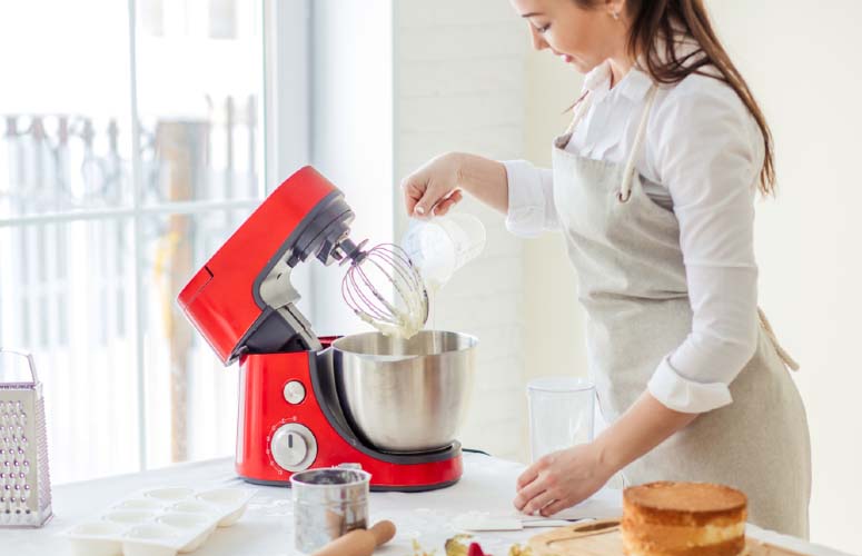 Kobieta w fartuchu napełnia metalową misę czerwonego robota do ciasta z rankingu.