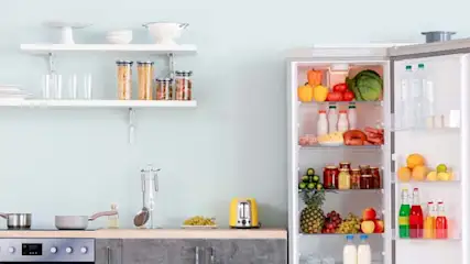 Kuchnia z otwartą lodówką, półkami i sprzętem AGD. Widoczne owoce, warzywa i naczynia.