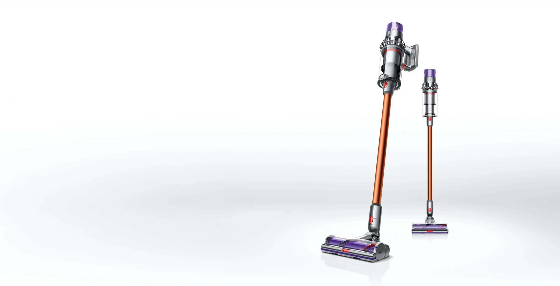 Dwa odkurzacze pionowe bezprzewodowe, jeden większy z przodu, drugi mniejszy z tyłu, oba w kolorze pomarańczowo-srebrno-fioletowym na białym tle.