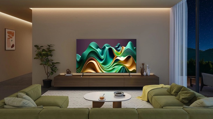 Pokój dzienny z zielonymi sofami, stolikiem kawowym i telewizorem wyświetlającym abstrakcyjny obraz. Za oknem widok na nocny krajobraz.