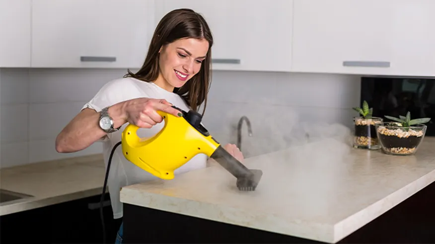 Kobieta czyści jasny blat za pomocą kompaktowej żółtej myjki parowej.