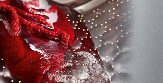 Czerwona tkanina w wodzie, wewnątrz bębna pralki ze stali nierdzewnej z otworami. Woda w ruchu.