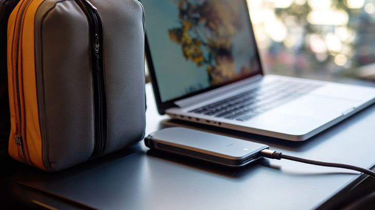 Laptop biurowy, obok niego leży powerbank i torba