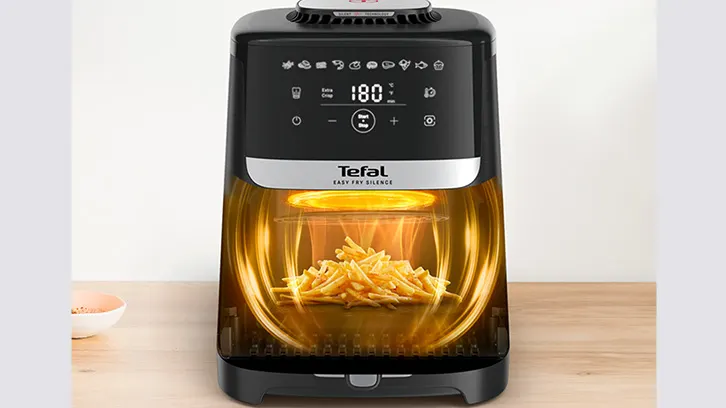 Czarny frytkownica beztłuszczowa Tefal z frytkami w środku, ustawiona na drewnianym stole. Na górze panel sterowania z wyświetlaczem.