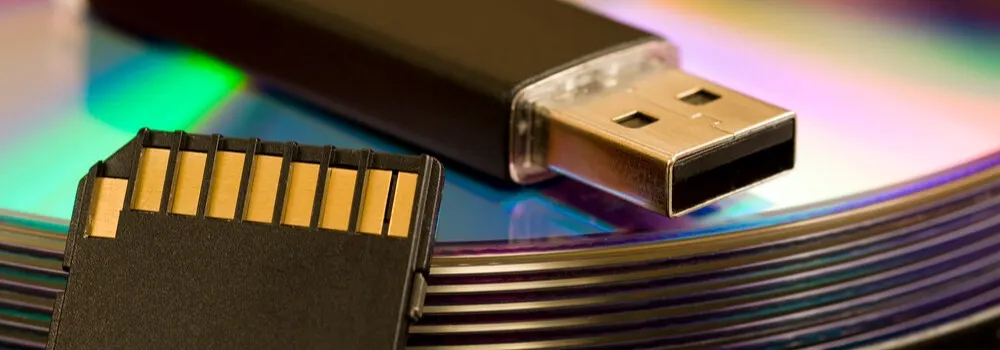 Czarny pendrive i karta pamięci leżą na stosie kolorowych płyt CD.