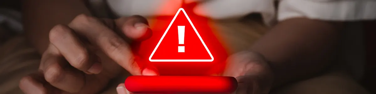 Grafika przedstawiająca mężczyznę z telefonem, który został zhakowany. Na pierwszym tle duży, czerwony wykrzyknik.