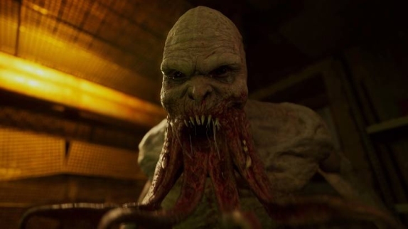 Na pierwszym planie widoczna jest postać z otwartymi ustami, z których wystają zęby i mięsiste wyrostki. Tło jest ciemne z żółtymi elementami.