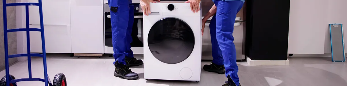 Dwóch mężczyzn ustawia i poziomuje pralkę stojącą w kuchni.