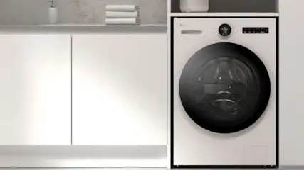 Wnętrze z pralką, szafkami i stołkiem barowym. W tle wazon z roślinami obok sofy. Minimalistyczny wystrój w jasnych odcieniach.