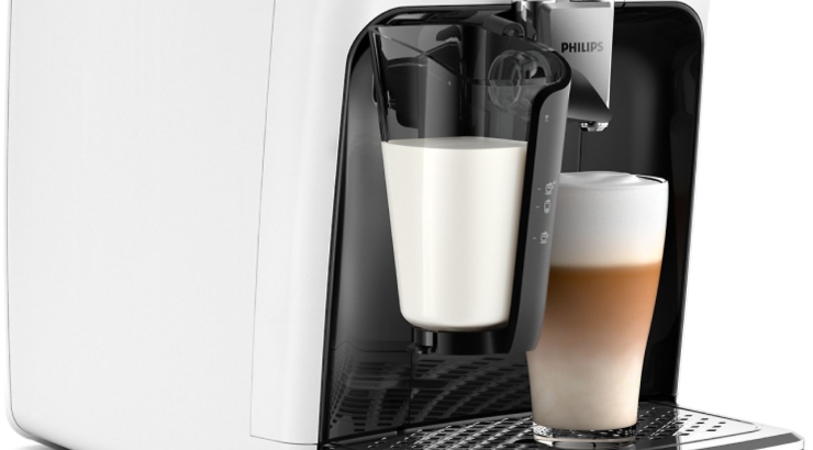 Ekspres do kawy w kolorze białym i czarnym. Obok szklanka z kawą latte i pojemnik z mlekiem.