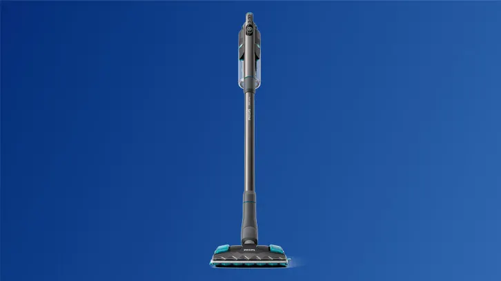 Na niebieskim tle stoi pionowo szary odkurzacz z turkusowymi akcentami na szczotce i uchwycie.