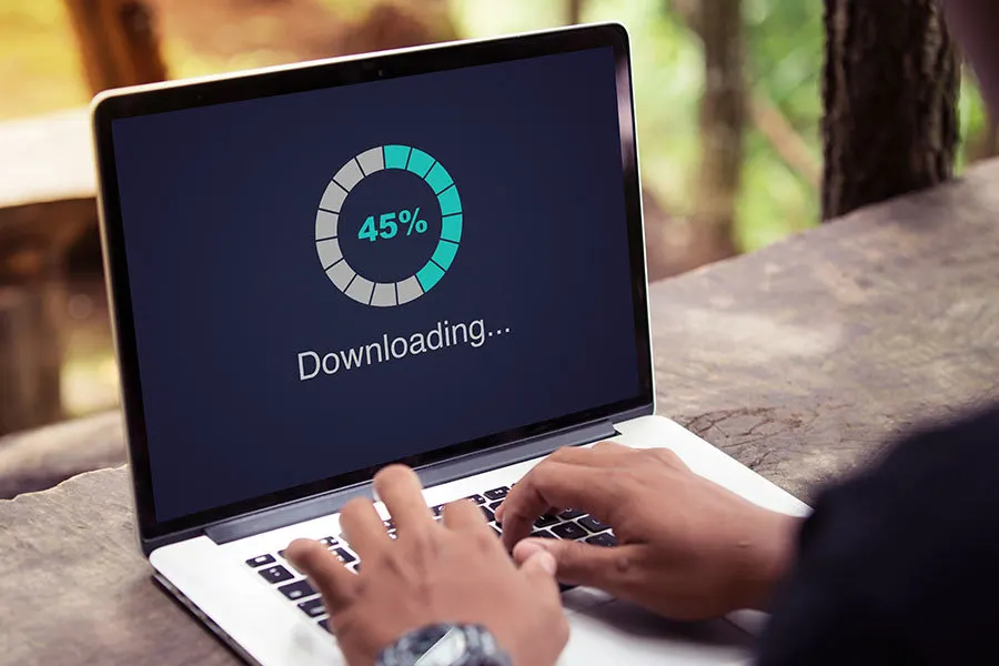 Osoba używa laptopa z ekranem pokazującym postęp pobierania na tle drzew.