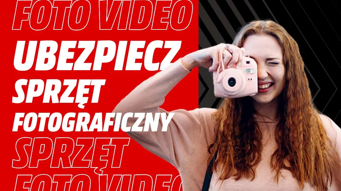 Kobieta trzyma różowy aparat, uśmiecha się. W tle czerwony napis: "FOTO VIDEO UBEZPIECZ SPRZĘT FOTOGRAFICZNY SPRZĘT".