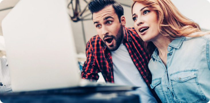 Para patrzy na laptop z zaskoczeniem. Mężczyzna w koszuli w kratę, kobieta w dżinsowej koszuli.