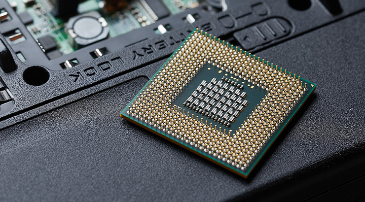 Procesor komputera na czarnym tle. Układ scalony z pinami jest kwadratowy i ma zielony obwód. Część płyty głównej widoczna w tle.