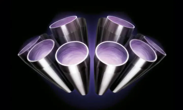 Srebrne, metalowe rury ułożone symetrycznie na ciemnym tle, skierowane otworami ku przodowi, wnętrze rur fioletowe.