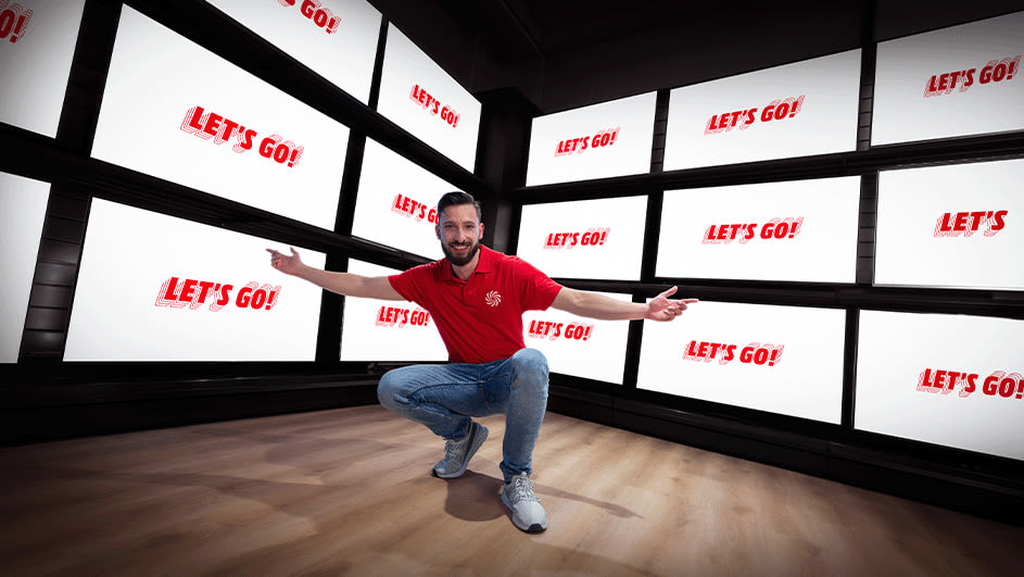 Mężczyzna w sklepie stacjonarnym MediaMarkt na tle telewizorów z napiem "Let's go!"