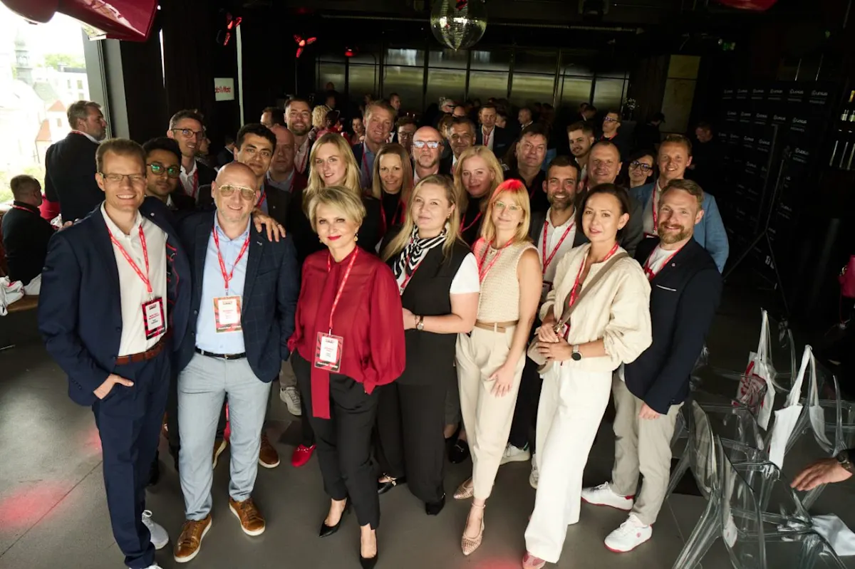 Grupa ludzi pozuje do zdjęcia w pomieszczeniu z dekoracyjną kulą dyskotekową. Wszyscy mają identyfikatory na szyjach.