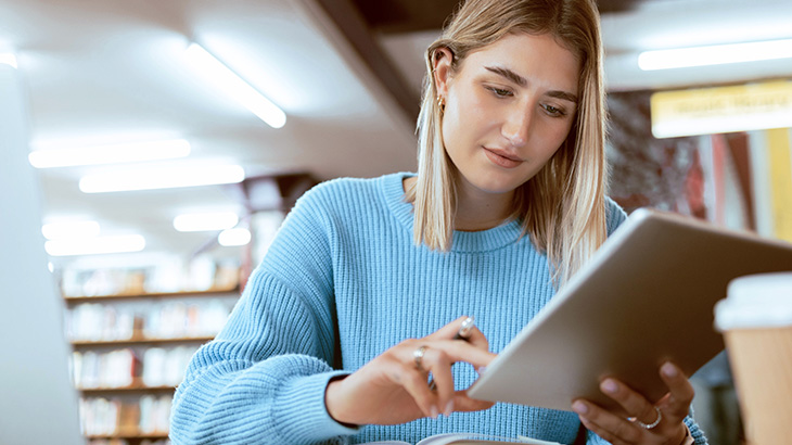 Kobieta w niebieskim swetrze korzysta z tabletu w bibliotece