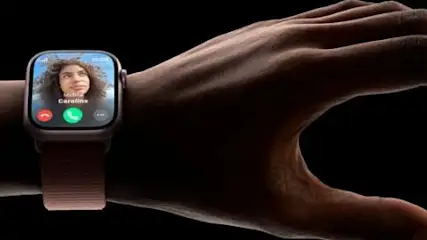 Na nadgarstku dłoni widoczny jest smartwatch z ekranem połączenia wideo, na którym widać osobę. Tło jest czarne.