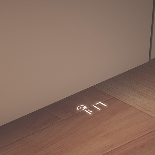 Na podłodze wyświetlony jest biały zegar cyfrowy. Podłoga jest brązowa, a ściana beżowa.