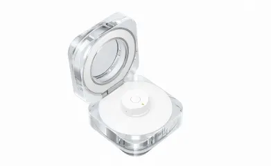 Otwarty, przezroczysty pojemnik z okrągłym lusterkiem w pokrywie i białym, okrągłym wkładem w środku.