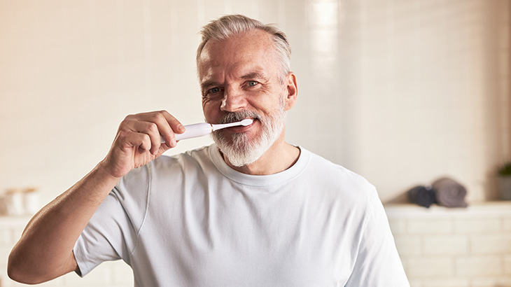 Dorosły mężczyzna łatwo i przyjemnie myje zęby szczoteczką elektryczną.