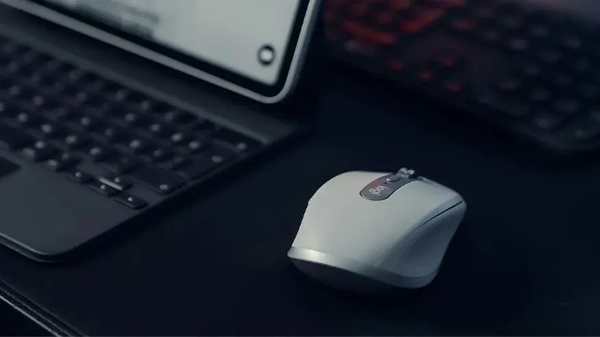 Biała mysz do pracy, profilowana, na ciemny biurku, obok laptopa.