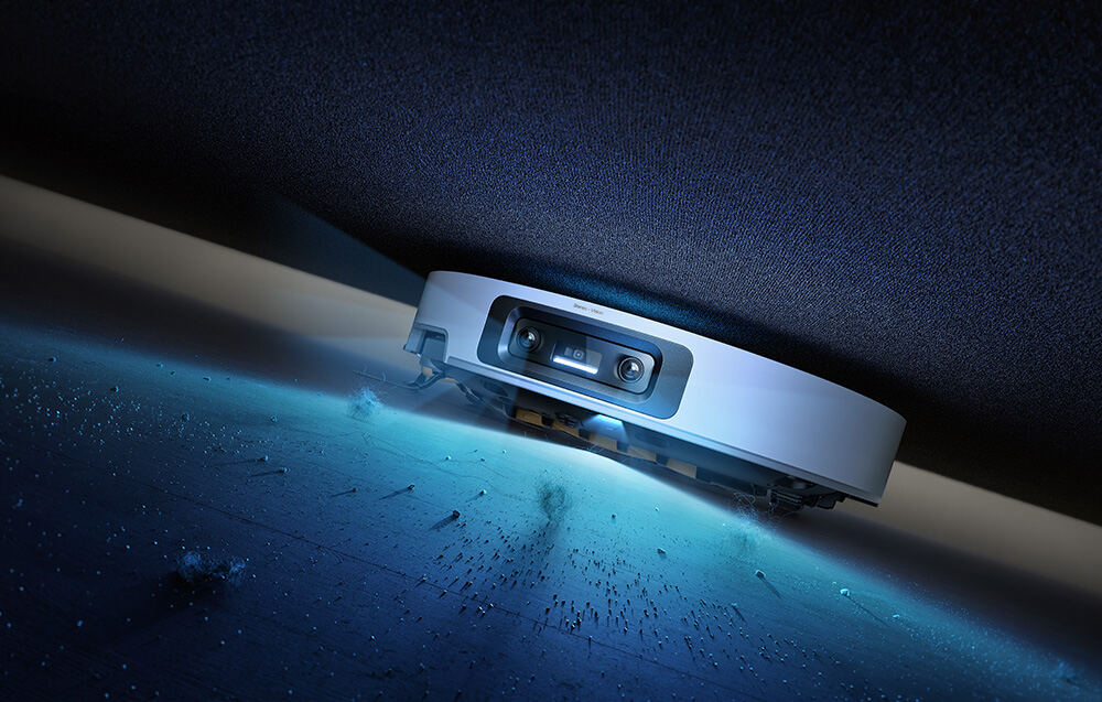 Na grafice znajduje się robot sprzątający, który w tym monecie odkurza pod łóżkiem, a jego światło podświetla bród, który sprząta robot.