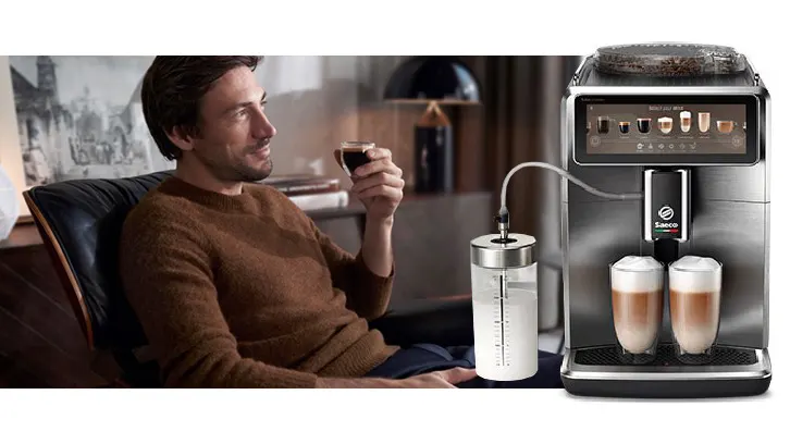 Mężczyzna pije kawę obok ekspresu Saeco, który przygotowuje latte macchiato. Obok widoczny pojemnik na mleko.