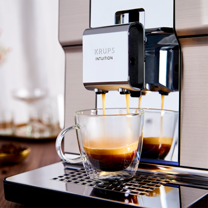 Ekspres Krups Intuition nalewa kawę do szklanki z podwójnymi ściankami. Kawa ma ciemny kolor i jest warstwowa.