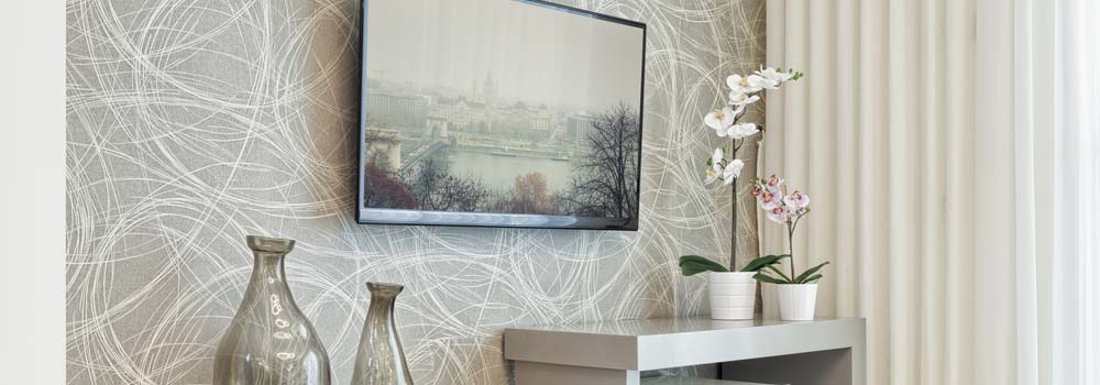 Dwa wazony, telewizor i dwa kwiaty na stoliku na tle ściany z wzorem i zasłony.