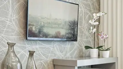 Dwa wazony, telewizor i dwa kwiaty na stoliku na tle ściany z wzorem i zasłony.