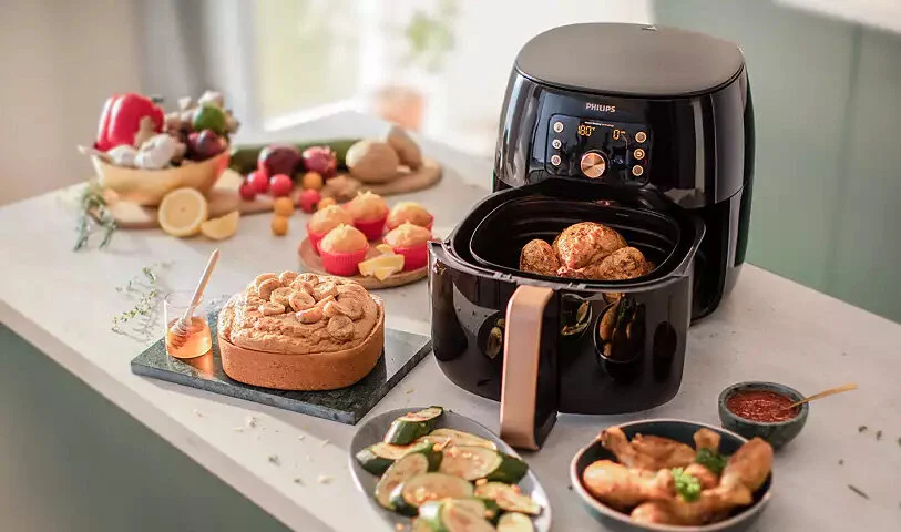 Frytkownica Philips na stole z potrawami, w tym ciastem, warzywami i mięsem.