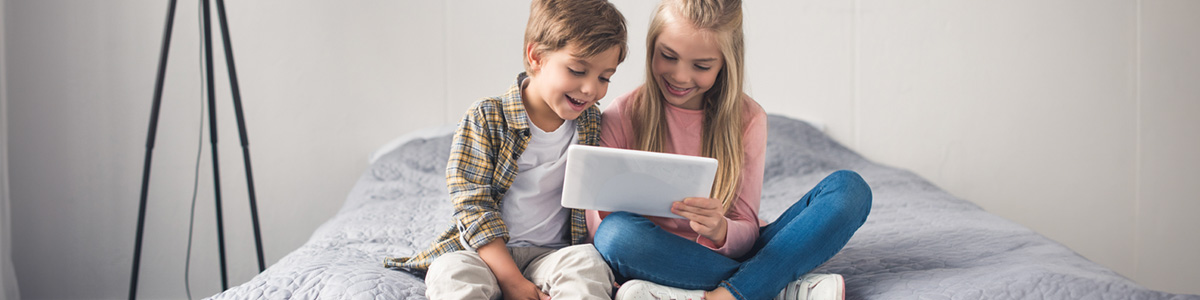 Dzieci siedzą na łóżku i patrzą na tablet.