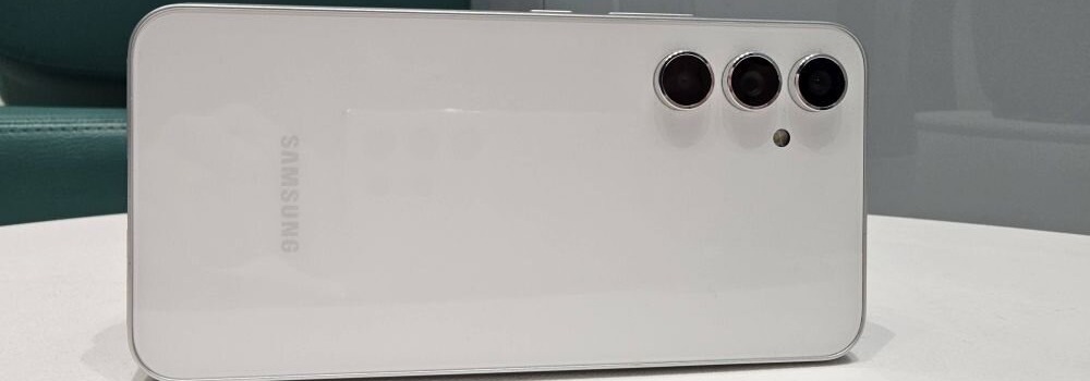 Biały smartfon Samsung z trzema obiektywami aparatu i napisem "Samsung" na obudowie leży na jasnej powierzchni.