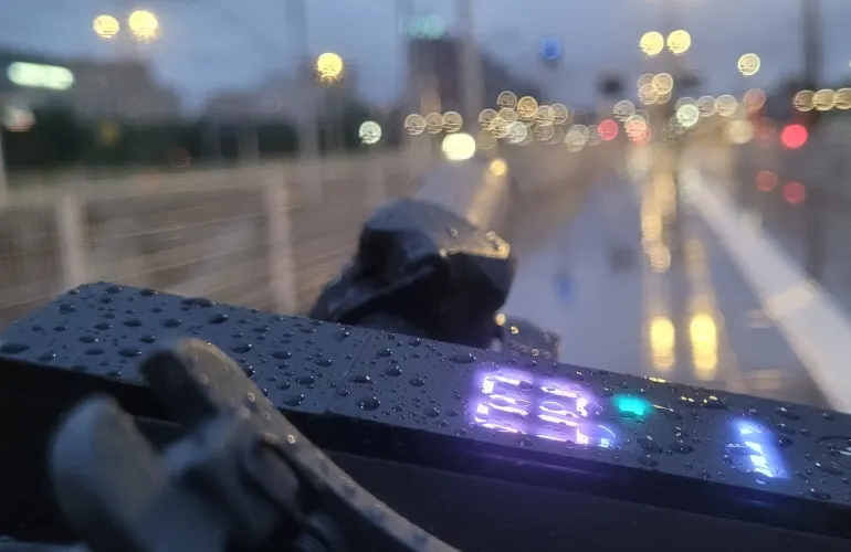 Na pierwszym planie czarny licznik z cyfrą 63, w tle mokra jezdnia i rozmyte światła miasta.