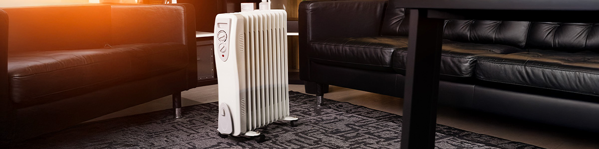 Biały grzejnik olejowy w pokoju z ciemnymi skórzanymi sofami.
