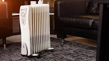 Biały grzejnik olejowy w pokoju z ciemnymi skórzanymi sofami.