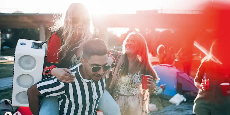 Grupa osób na zewnątrz, w tle budynki. Mężczyzna w okularach nosi głośnik. Inni trzymają czerwone kubki.