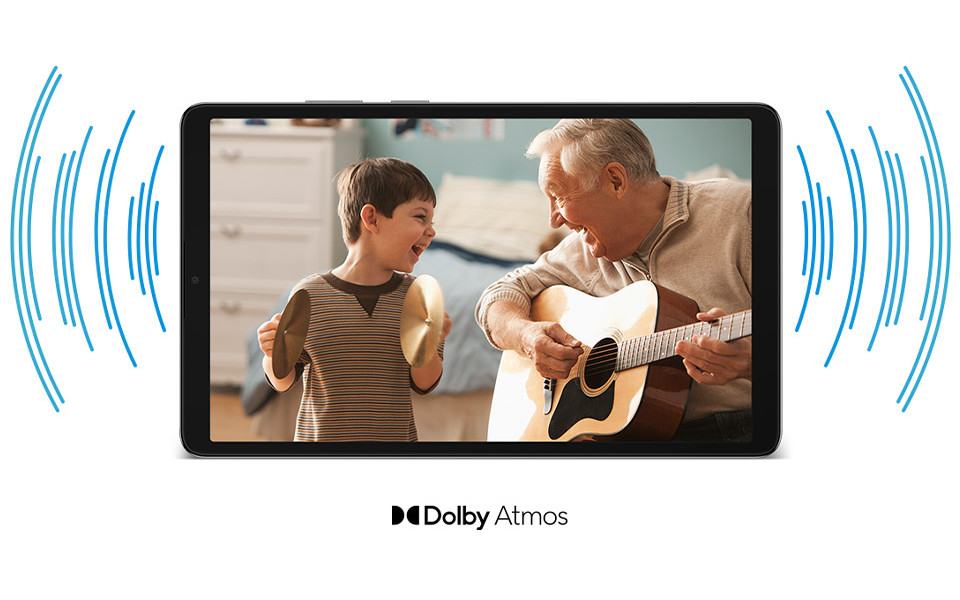 Tablet wyświetlający scenę z dwoma osobami - młodym chłopcem i starszym mężczyzną grającym na gitarze, w tle domowe wnętrze. Obrazek jest otoczony graficznymi falami dźwiękowymi po obu stronach, z napisem "Dolby Atmos" poniżej.