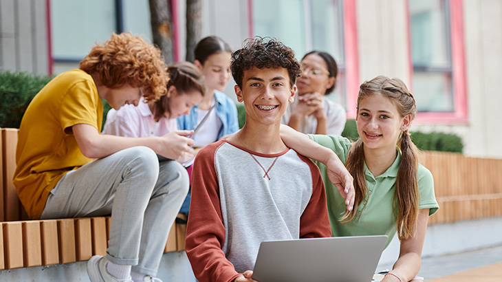 6 młodych osób siedzi na schodach, jedna z nich ma laptopa