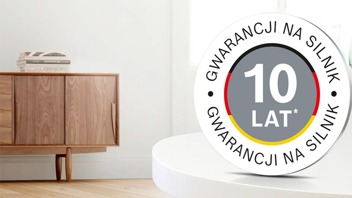Na pierwszym planie okrągła naklejka "10 lat gwarancji na silnik", w tle drewniana komoda z książkami.
