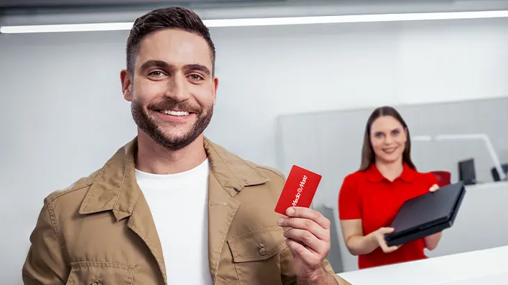 Mężczyzna trzymający kartę podarunkową, w tle kobieta pracująca w MediaMarkt.