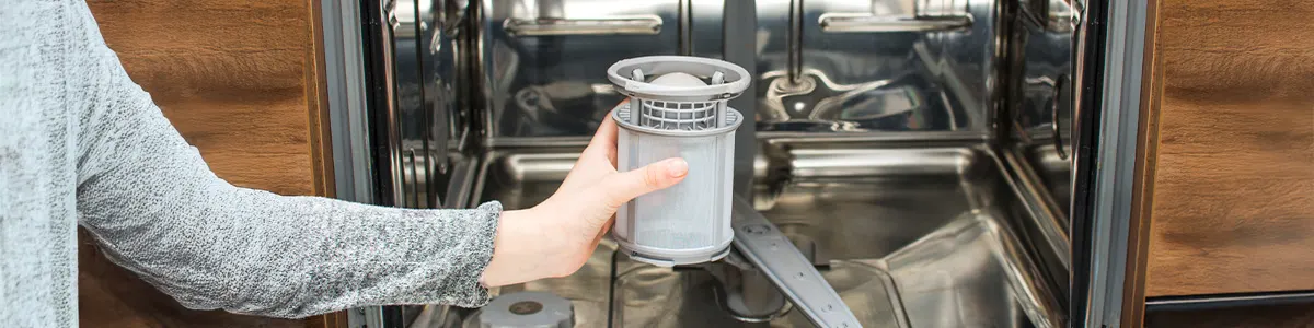 Kobieta w niebieskich rękawicach czyści metalową zmywarkę w jasnej kuchni.