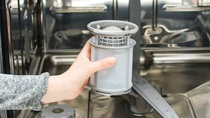 Kobieta w niebieskich rękawicach czyści metalową zmywarkę w jasnej kuchni.