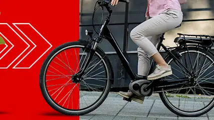 Czerwone tło z białą strzałką, słoik z monetami i rośliną. Rowerzysta na czarnym rowerze na tle budynku.