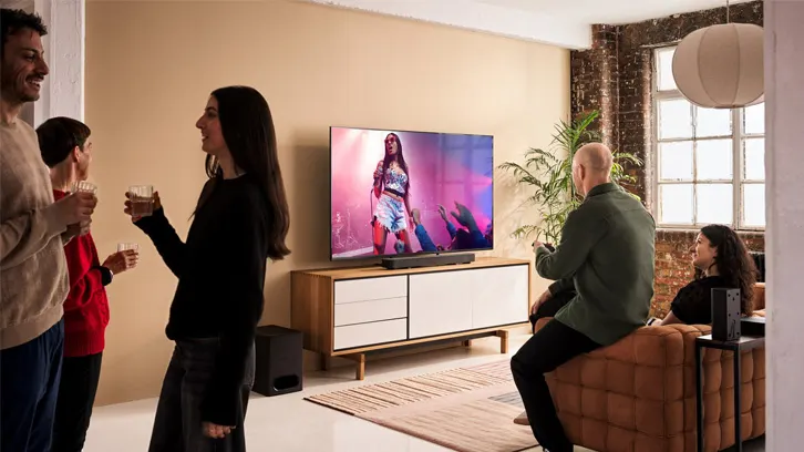 Trzy osoby rozmawiające w mieszkaniu, a dwie oglądające telewizję